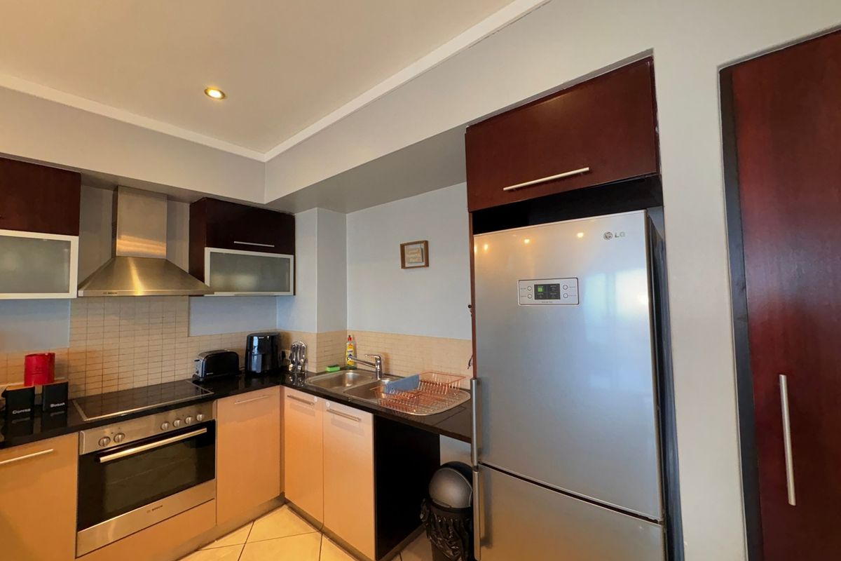A functional kitchen featuring dark wood cabinetry, granite countertops, a stainless steel oven, hob, and extractor fan with tiled backsplash and neutral floor tiles.