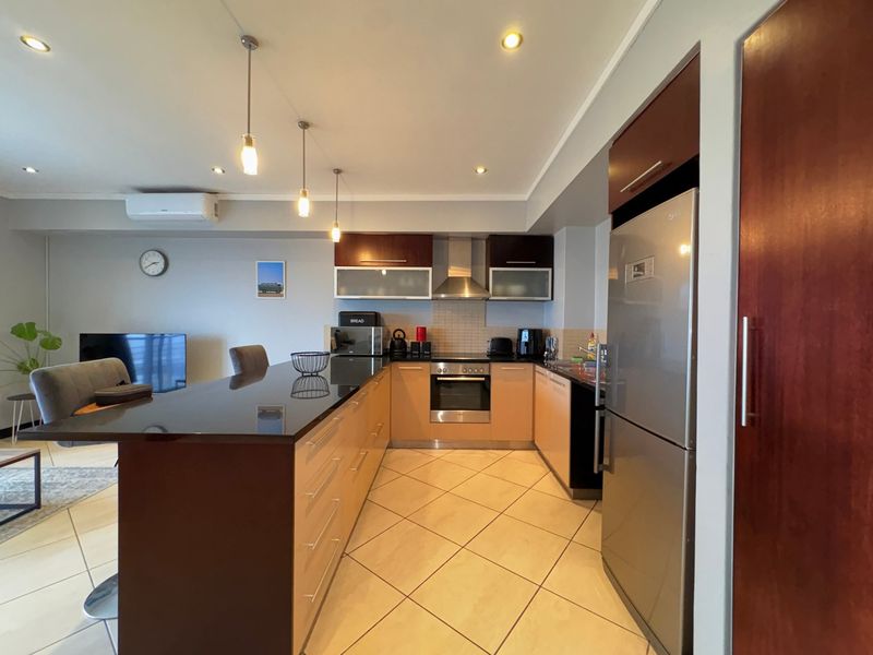 Modern open-plan kitchen featuring dark granite countertops, ample built-in cabinetry, stainless steel appliances, and tiled flooring, seamlessly integrated with the living area.