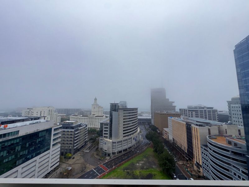 An elevated city skyline view captured from an apartment balcony on a cloudy day.