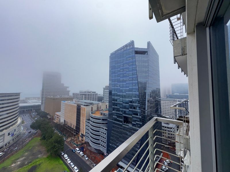 An elevated city skyline view captured from a balcony, showcasing surrounding high-rise commercial buildings and urban infrastructure.
