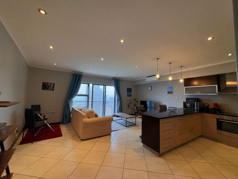 Spacious open-plan living area featuring a modern kitchen with an island, tiled floors, recessed lighting, and direct access to a balcony through sliding doors.