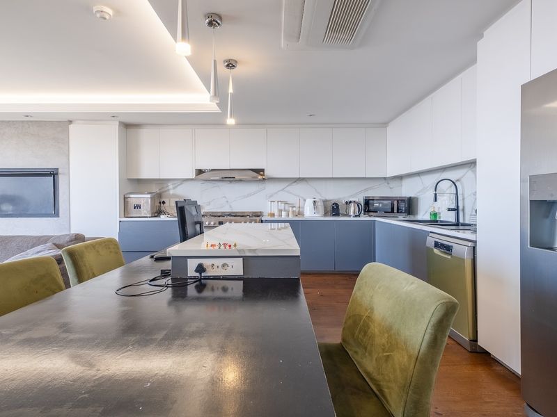 Modern open-plan living and kitchen area featuring sleek cabinetry, stone countertops, integrated appliances, recessed lighting, and a built-in fireplace.