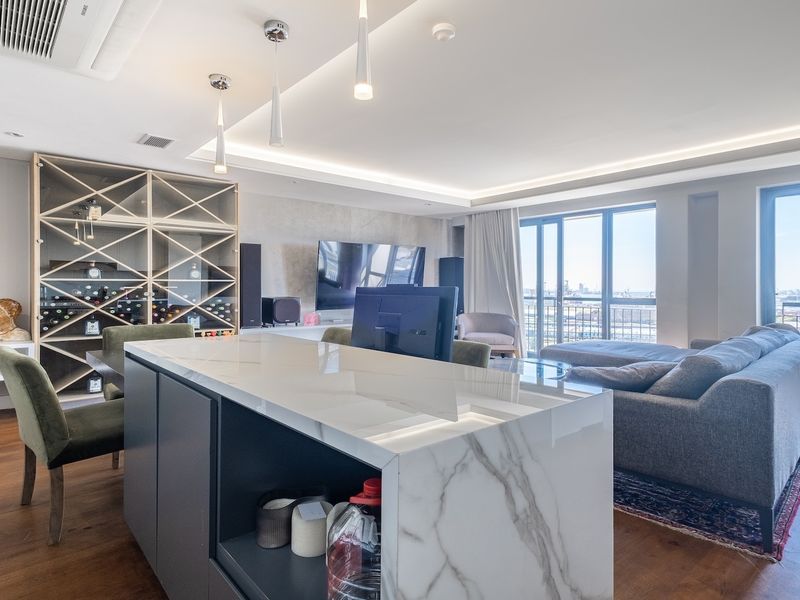 Modern open-plan living area featuring a marble kitchen island, recessed lighting, hardwood floors, and large sliding doors leading to a balcony with city views.