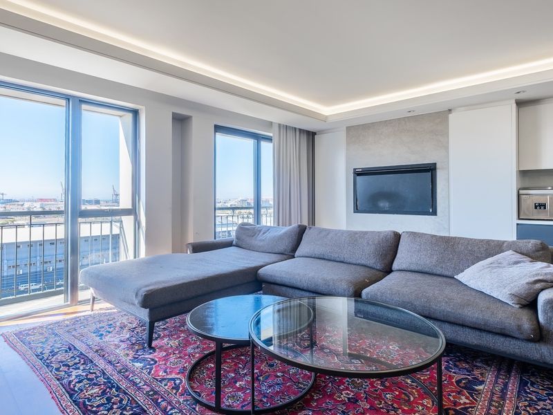 Modern open-plan living area featuring hardwood floors, recessed ceiling lighting, a built-in fireplace, and large sliding doors opening to a balcony with city views.