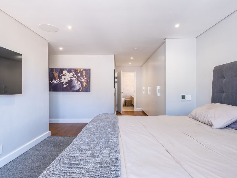 Modern bedroom featuring built-in cupboards, recessed ceiling lighting, and a mix of hardwood and carpeted flooring, with an en-suite bathroom visible.
