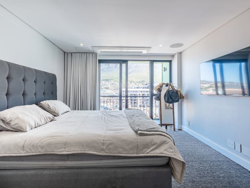 Modern bedroom featuring plush carpeting, ducted air conditioning, recessed lighting, and a sliding glass door leading to a balcony with city views.