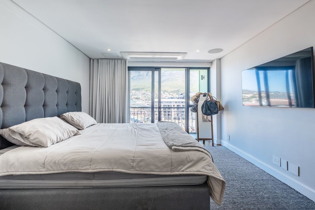 Modern bedroom featuring plush carpeting, ducted air conditioning, recessed lighting, and a sliding glass door leading to a balcony with city views.
