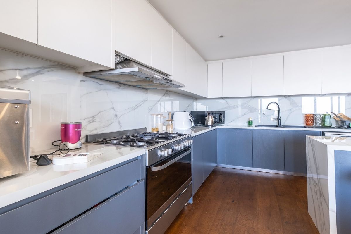 Modern kitchen featuring sleek two-tone cabinetry, marble-look splashbacks, high-quality quartz countertops, gas cooktop, and integrated appliances with warm hardwood flooring.