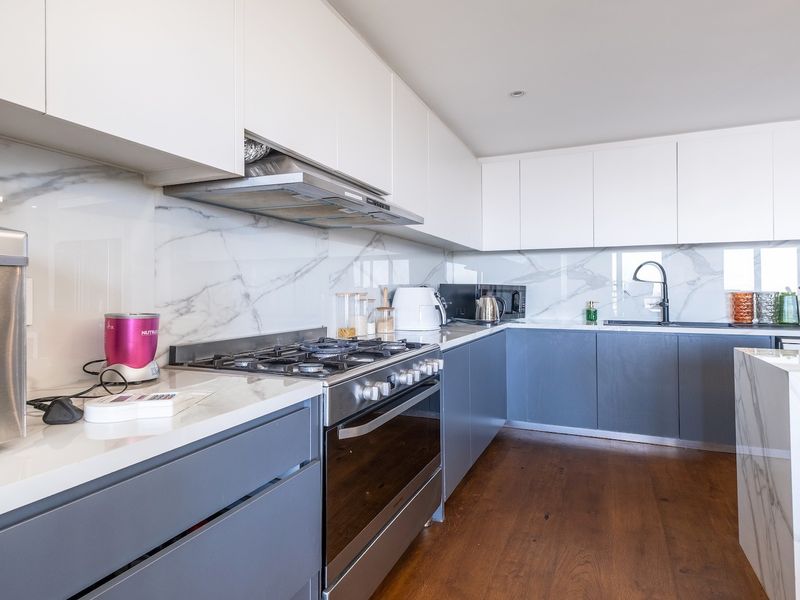 Modern kitchen featuring sleek two-tone cabinetry, marble-look splashbacks, high-quality quartz countertops, gas cooktop, and integrated appliances with warm hardwood flooring.