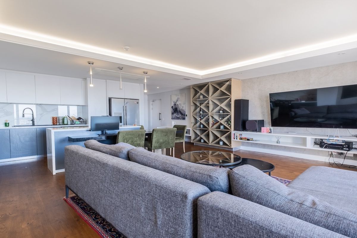 Modern open-plan living area featuring a sleek kitchen with stone island, built-in wine storage, floating media console, and recessed ceiling lighting throughout.
