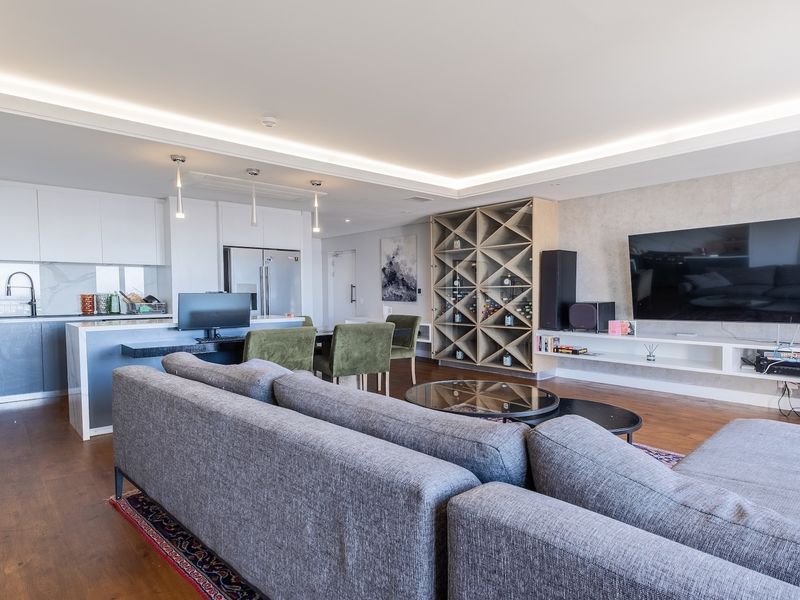 Modern open-plan living area featuring a sleek kitchen with stone island, built-in wine storage, floating media console, and recessed ceiling lighting throughout.