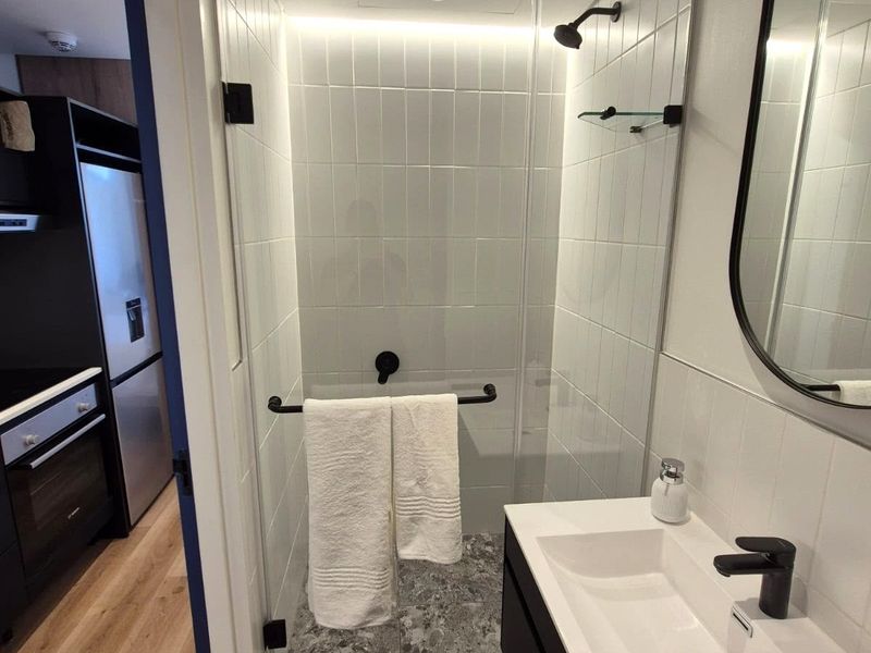 Modern bathroom featuring a walk-in shower with glass screen, contemporary black tapware, vanity basin, and stylish tiled finishes.