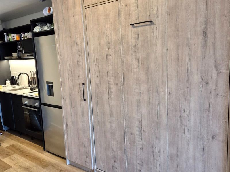 Modern kitchen featuring sleek dark cabinetry, integrated appliances, wood-look laminate flooring, and efficient under-cabinet lighting.