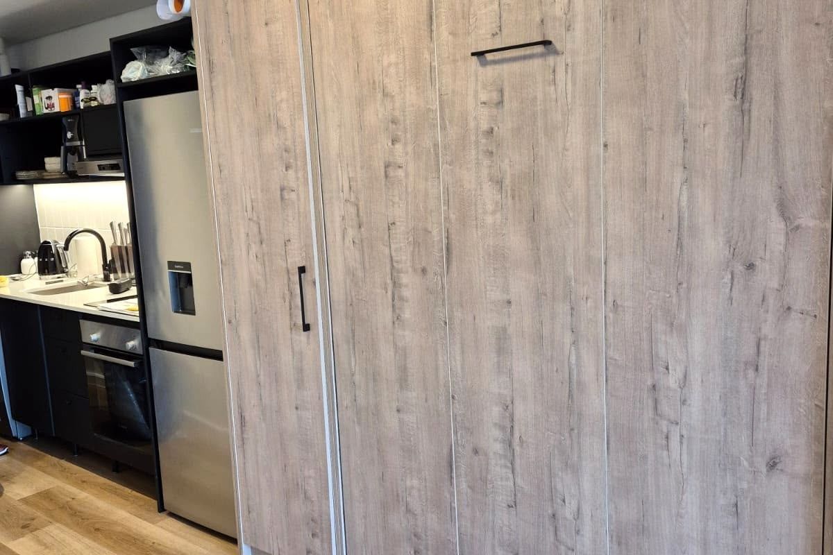 Modern kitchen featuring sleek dark cabinetry, integrated appliances, wood-look laminate flooring, and efficient under-cabinet lighting.