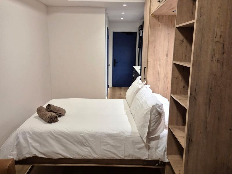 A modern bedroom featuring built-in wooden cabinetry, recessed ceiling lighting, and neutral finishes, creating a functional and contemporary living space.