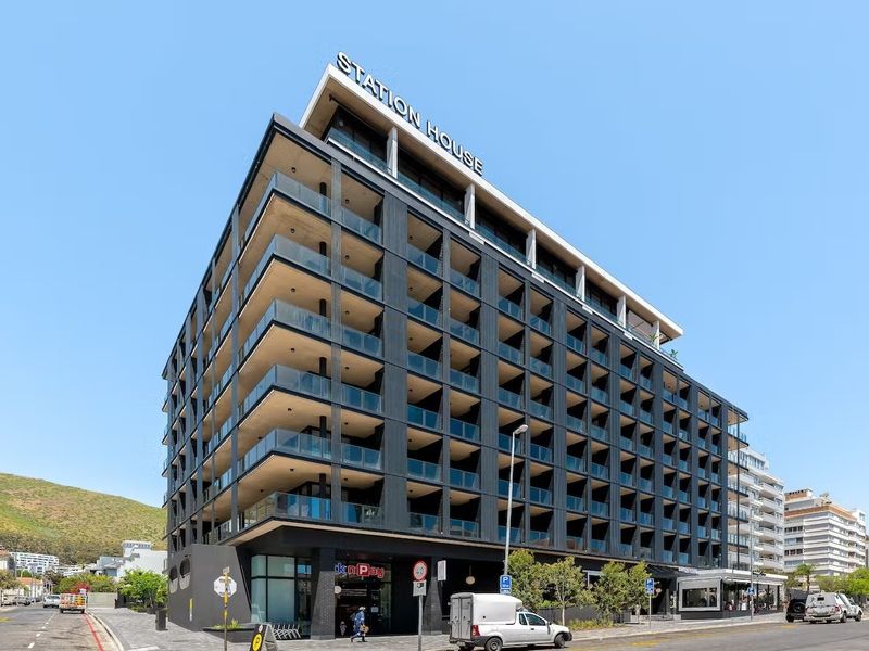 Modern multi-story apartment building featuring a contemporary dark facade, glass-fronted balconies, and ground-floor commercial space in a prime urban location.