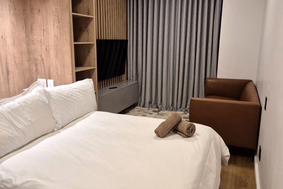 A modern bedroom featuring custom timber-look wall paneling, integrated shelving, a built-in media console, and floor-to-ceiling curtains.