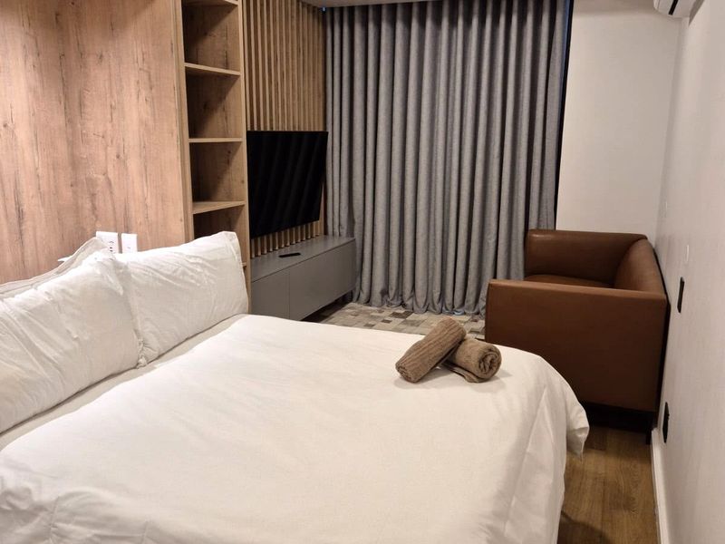A modern bedroom featuring custom timber-look wall paneling, integrated shelving, a built-in media console, and floor-to-ceiling curtains.