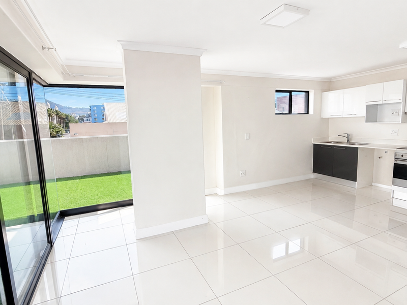 Modern open-plan kitchen and living area featuring sleek cabinetry, integrated appliances, polished floor tiles, and large sliding doors opening to a private balcony.