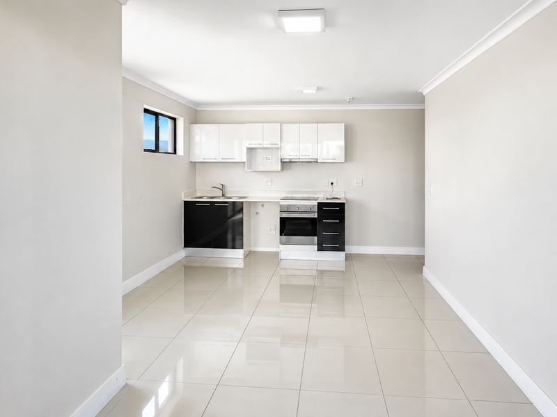 A clean, modern kitchen featuring high-gloss cabinetry, integrated oven and hob, and neutral tiled flooring in an open-plan layout.