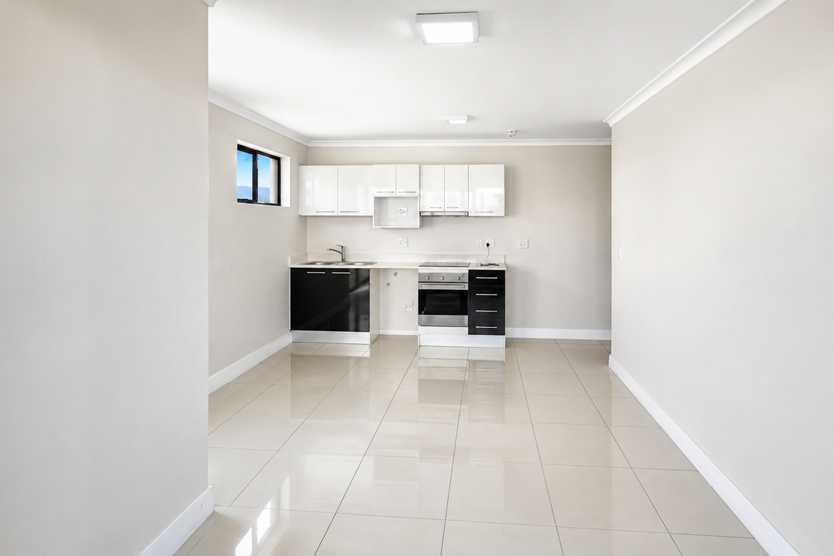 A clean, modern kitchen featuring high-gloss cabinetry, integrated oven and hob, and neutral tiled flooring in an open-plan layout.