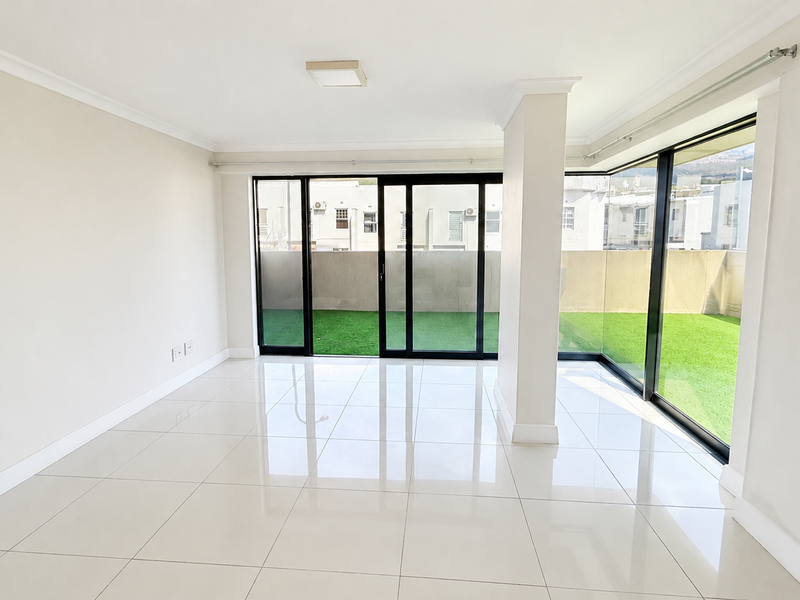 A bright, empty living area featuring large sliding glass doors that open onto a private balcony with artificial grass.
