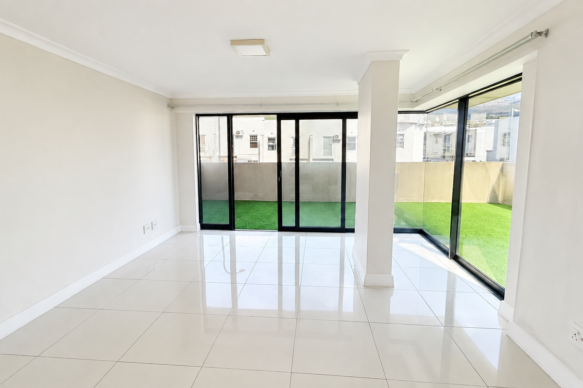 A bright, empty living area featuring large sliding glass doors that open onto a private balcony with artificial grass.