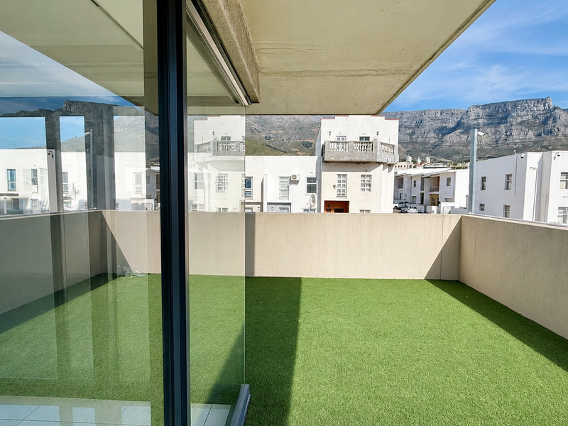 Spacious balcony featuring artificial grass flooring, enclosed by a concrete balustrade, offering clear views of the surrounding neighborhood and mountain range.