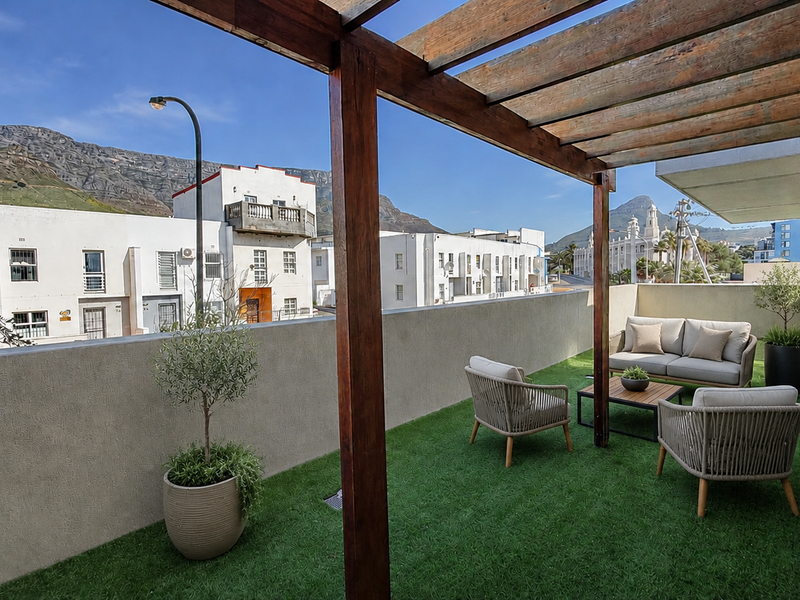 A spacious balcony featuring a timber pergola, artificial grass flooring, and a masonry parapet wall, offering scenic mountain and neighborhood views.