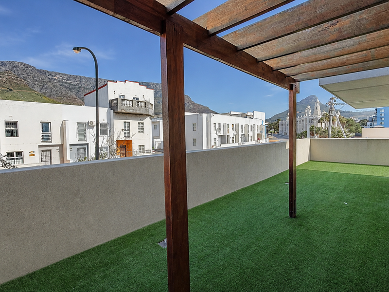 Spacious balcony featuring a wooden pergola, artificial grass flooring, and a solid parapet wall with scenic mountain and neighbourhood views.