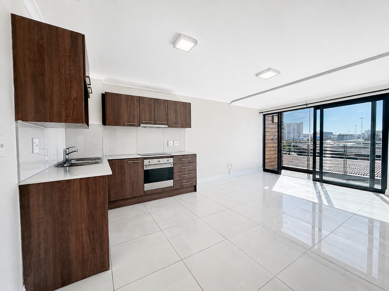 Modern open-plan kitchen and living area featuring dark wood cabinetry, stone countertops, integrated appliances, and large sliding doors leading to a balcony.