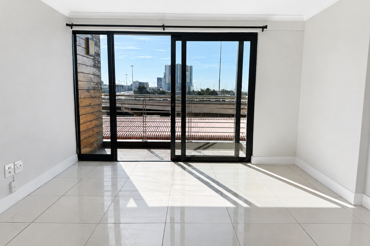 A bright, empty living room featuring large sliding glass doors that open onto a balcony, with polished floor tiles and neutral wall finishes.
