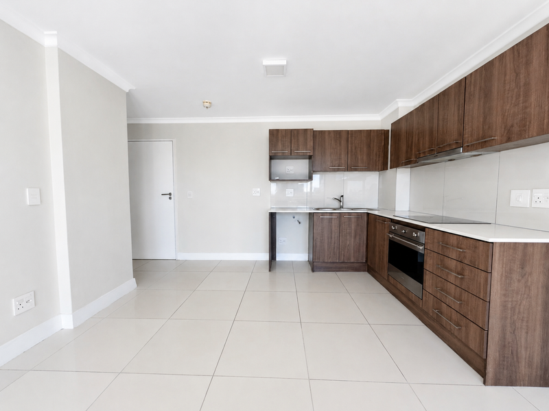 Modern kitchen featuring dark wood cabinetry, stone countertops, integrated oven, electric hob, and tiled flooring in a clean, open-plan layout.