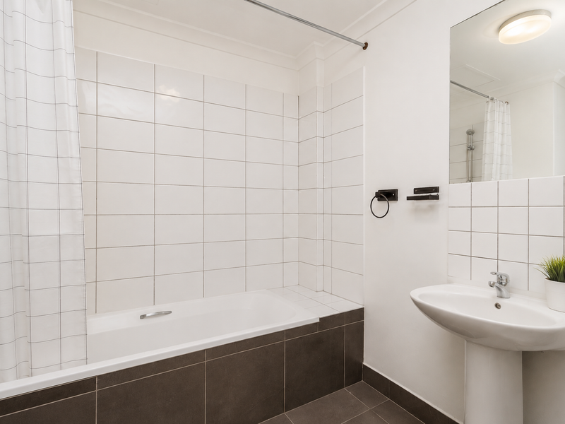 A clean, functional bathroom featuring a pedestal basin, a built-in bathtub with tiled surround, and a wall-mounted mirror.