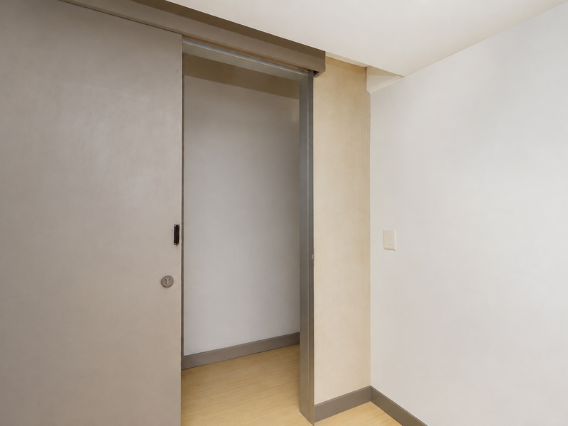 A clean, minimalist hallway featuring a modern sliding door, neutral wall finishes, and light-toned laminate flooring.