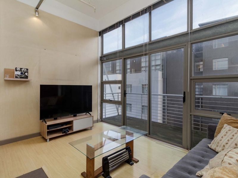 Spacious living room featuring double-height windows, laminate flooring, and direct access to a private balcony, offering ample natural light.