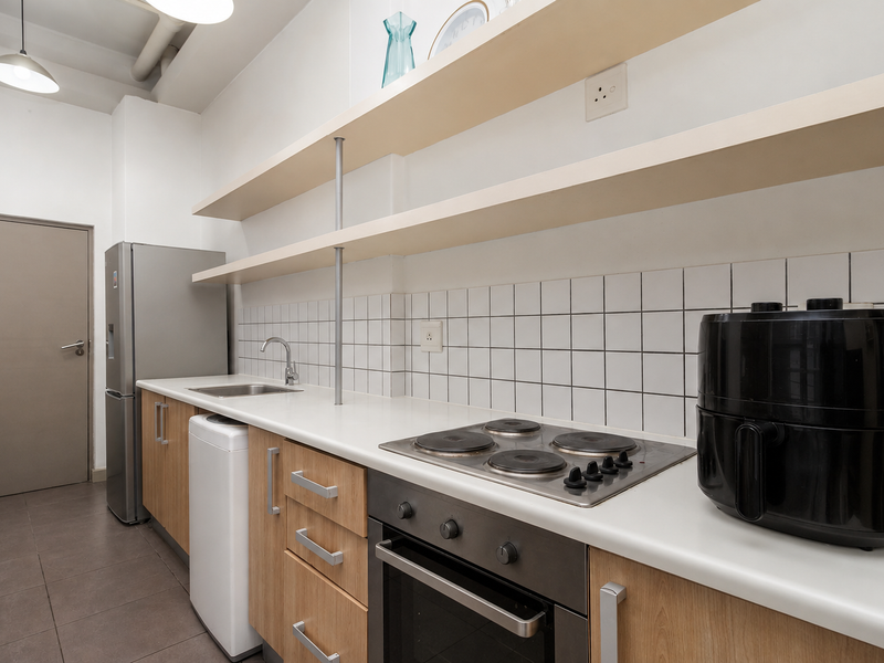 A functional kitchen featuring light wood cabinetry, open shelving, a tiled backsplash, and integrated electric cooking appliances.