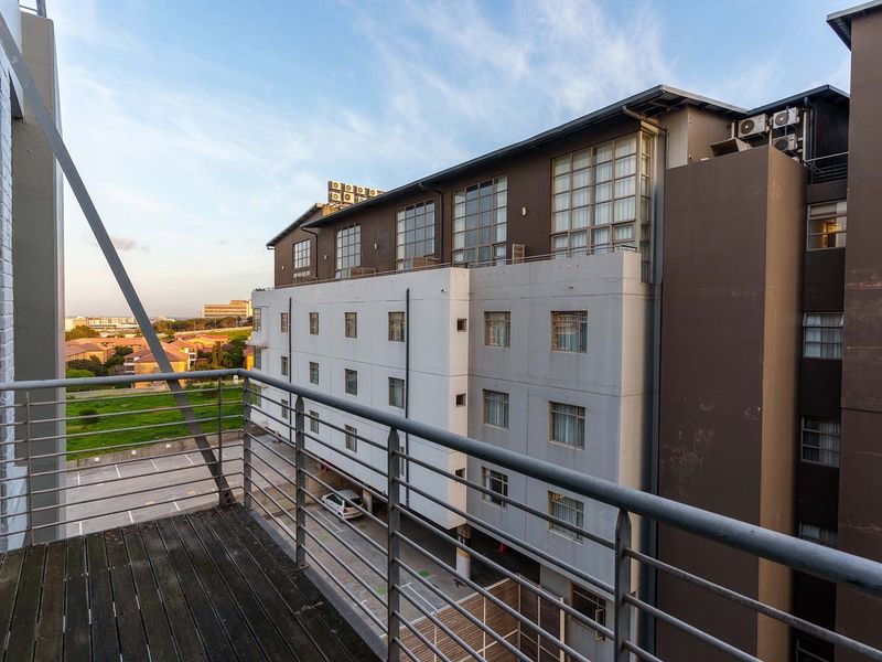 A balcony featuring timber decking and metal railings, offering an elevated view of the surrounding apartment complex and parking area.