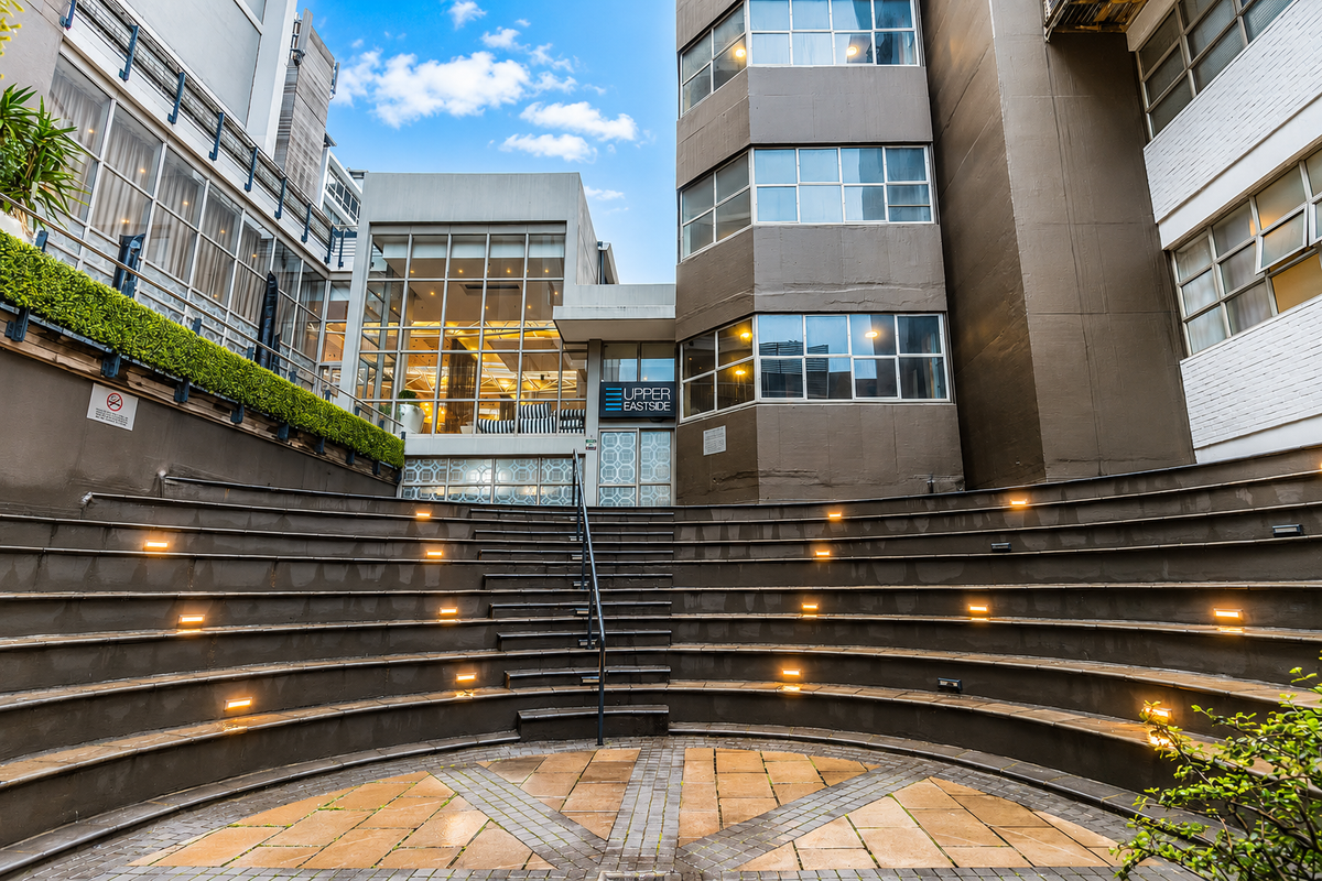 A modern apartment complex courtyard featuring a tiered amphitheatre seating area with integrated lighting and paved ground surfaces.