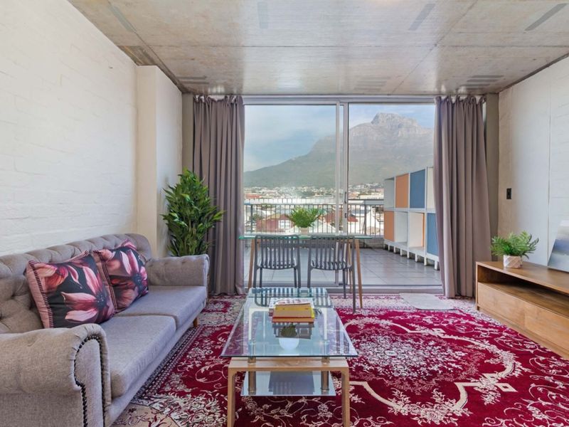 A bright living room featuring an exposed concrete ceiling, painted brick walls, and large sliding doors opening onto a balcony with mountain views.