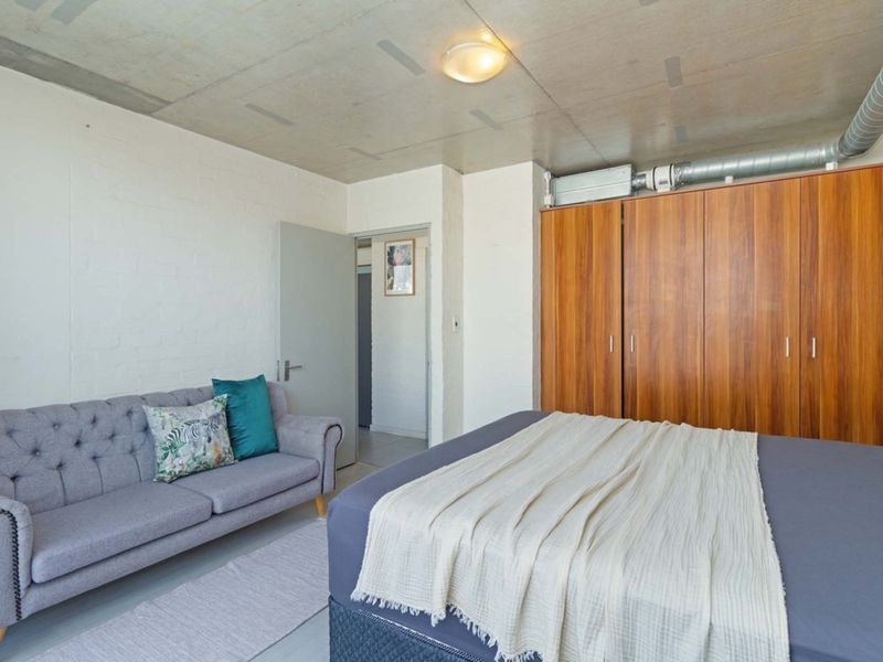 A bedroom featuring an exposed concrete ceiling, industrial-style ventilation ducting, and a large built-in wooden wardrobe.