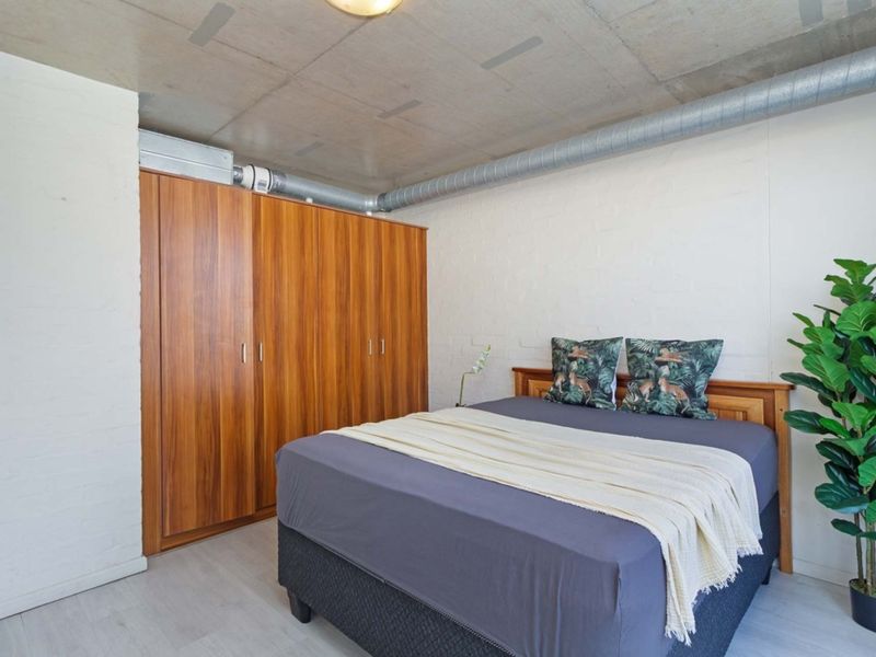 A bedroom featuring an industrial aesthetic with an exposed concrete ceiling, exposed ducting, and a large built-in wooden wardrobe.