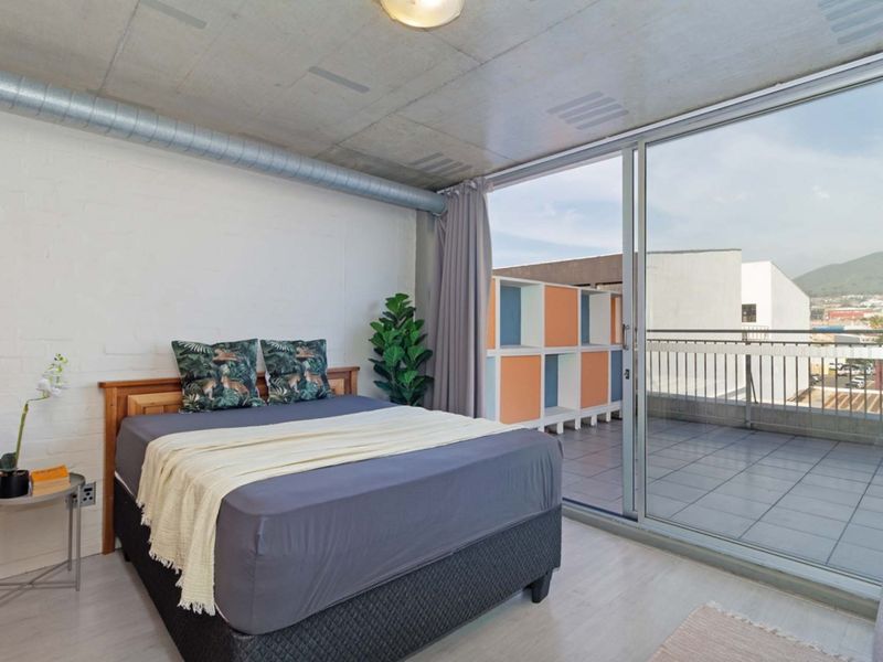 Modern bedroom featuring an industrial aesthetic with an exposed concrete ceiling, ducting, and large sliding glass doors leading to a private balcony.