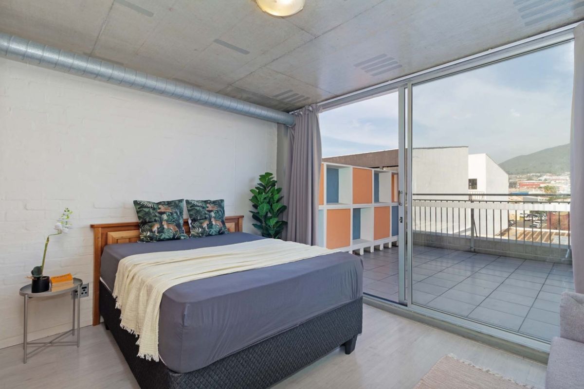Modern bedroom featuring an industrial aesthetic with an exposed concrete ceiling, ducting, and large sliding glass doors leading to a private balcony.