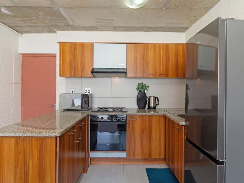 Compact kitchen featuring wood veneer cabinetry, granite countertops, built-in oven with hob, extractor fan, and an industrial-style exposed concrete ceiling.