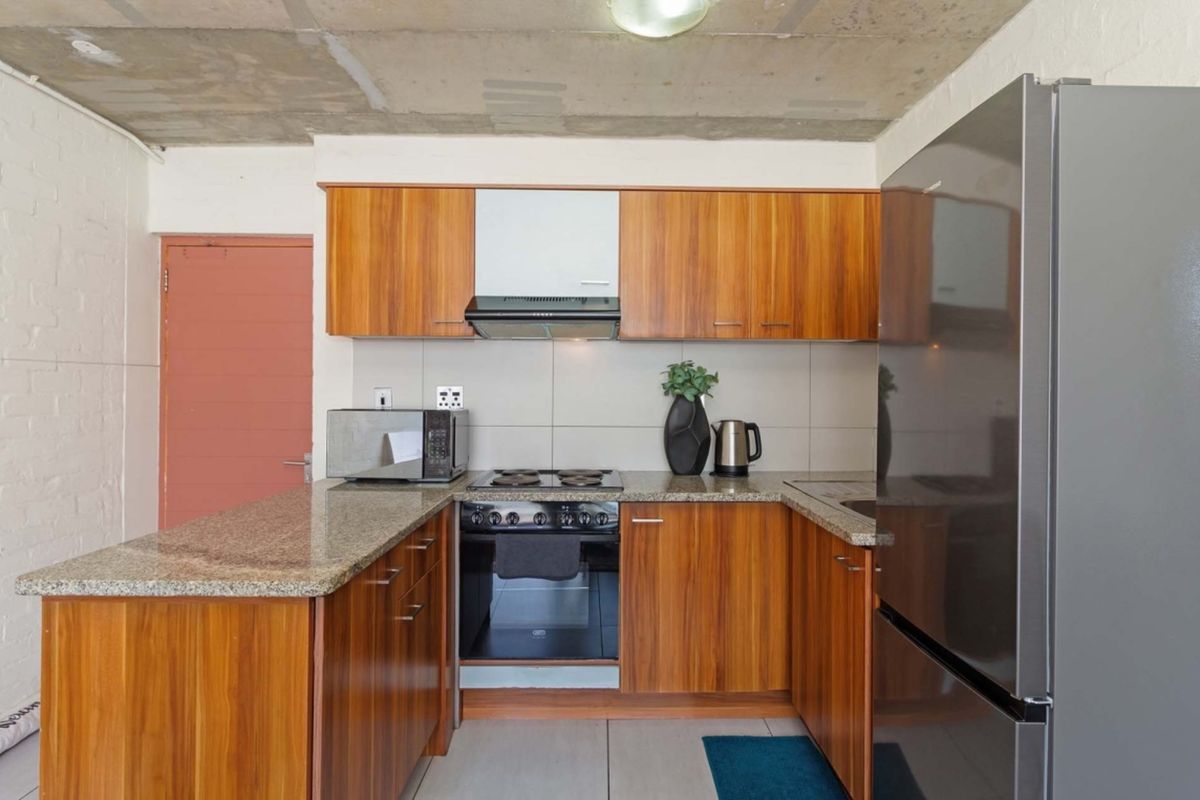 Compact kitchen featuring wood veneer cabinetry, granite countertops, built-in oven with hob, extractor fan, and an industrial-style exposed concrete ceiling.