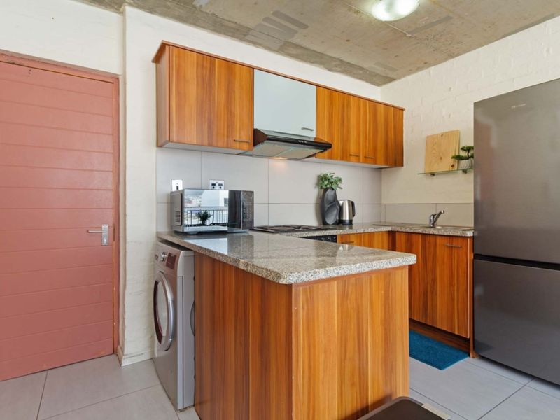 Compact kitchen featuring wooden cabinetry, granite countertops, an extractor fan, and an exposed concrete ceiling, offering a modern industrial aesthetic.