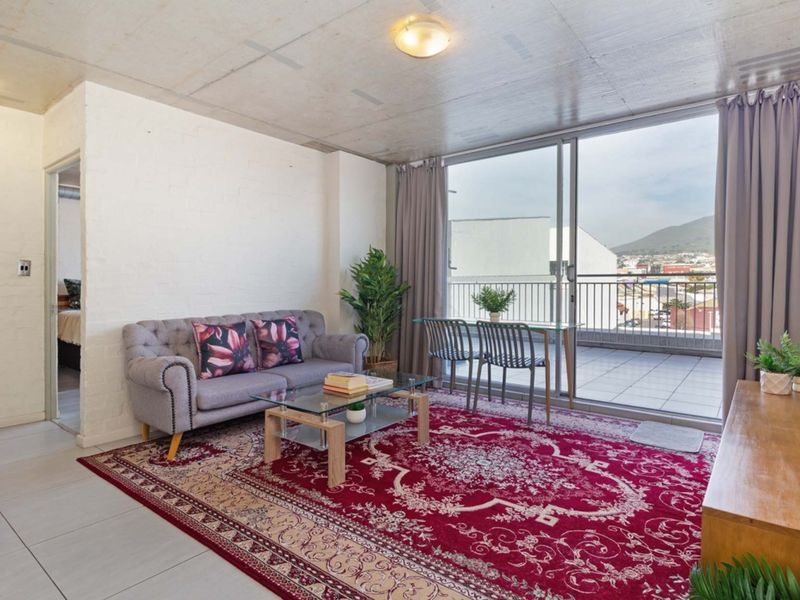 Open-plan living area featuring exposed concrete ceilings, tiled floors, and large sliding glass doors leading to a private balcony with urban views.