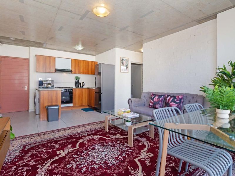 Open-plan living and kitchen area featuring exposed concrete ceilings, tiled flooring, and a functional kitchen with built-in cabinetry and appliances.