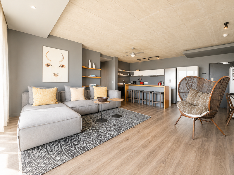 Modern open-plan living area featuring an exposed concrete ceiling, laminate flooring, and a sleek kitchen with a breakfast bar island.